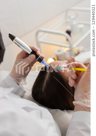 Woman receives microneedling and injections for hair growth scalp therapy in trichology clinic 129440321