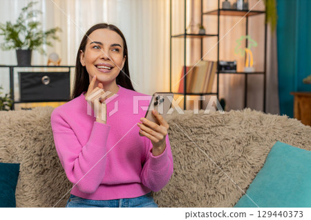 Young woman on sofa browsing online store on mobile phone enthusiastically selecting products 129440373