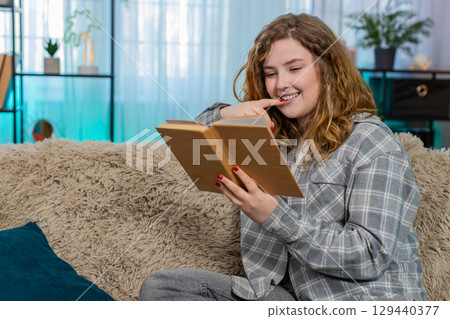 Woman sitting on sofa opening and reading book with focus thoughtfully flipping pages and reflecting 129440377