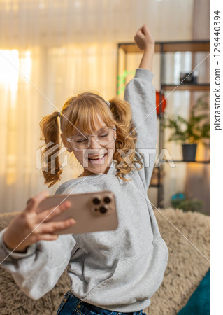 Young teenager girl playing mobile game at home sofa celebrate victory win, cheerful triumph moment 129440394