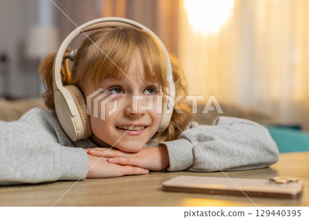 Young girl listening to audiobook with headphones, excitedly reacting to story with open eyes, smile 129440395