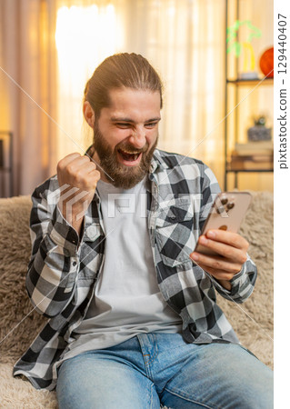 Young man scrolling social media at home, sudden lottery win, joy, amazing phone triumph victory Young man scrolling social media at home, sudden lottery win, joy, amazing phone triumph victory 129440407