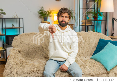 Upset unhappy young Indian man showing thumbs down sign gesture, expressing discontent at home 129440452