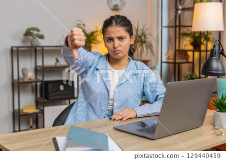 Upset unhappy woman freelancer showing thumbs down gesture, expressing discontent sitting at table 129440459