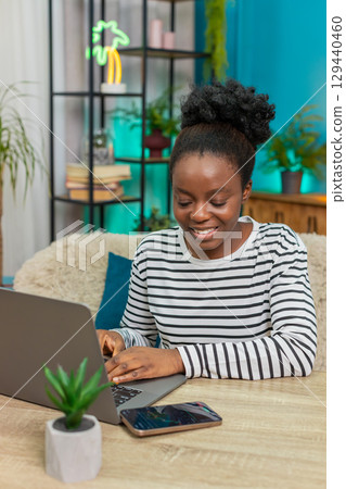 African American woman analyzing cryptocurrency charts laptop table phone indoors focused notes 129440460
