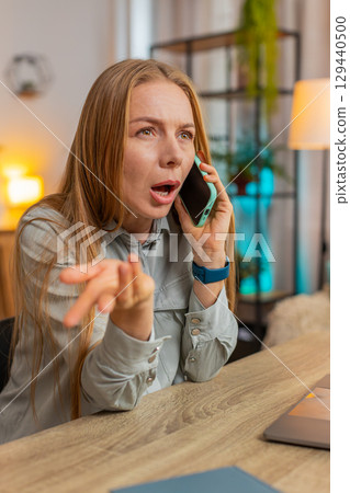 Angry Caucasian mature businesswoman freelancer talking on smartphone sitting at home office table Angry Caucasian mature businesswoman freelancer talking on smartphone sitting at home office table 129440500
