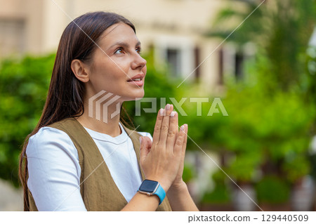 Young European woman praying with closed eyes to god asking for blessing, help, forgiveness outdoors 129440509