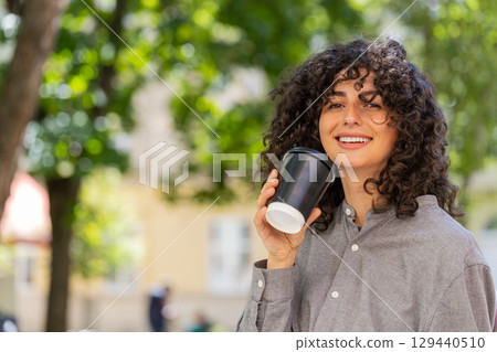 Happy young woman enjoying drinking morning coffee hot drink relaxing taking a break on city street 129440510