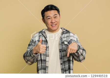 Asian blogger man pointing down, saying to subscribe gesturing ok like showing place for information Asian blogger man pointing down, saying to subscribe gesturing ok like showing place for information 129440519