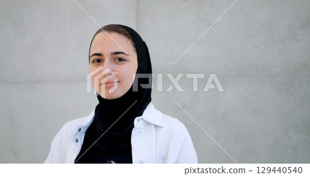Muslim woman in hijab displaying varied facial expressions from contemplative to intense, standing against minimalist concrete wall backdrop Muslim woman in hijab displaying varied facial expressions from contemplative to intense, standing against minimalist concrete wall backdrop 129440540