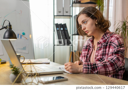 Business woman working on laptop computer online, writing notes in planner notebook at office Business woman working on laptop computer online, writing notes in planner notebook at office 129440617