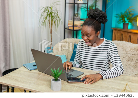African American woman analyzing cryptocurrency charts laptop table phone indoors focused notes African American woman analyzing cryptocurrency charts laptop table phone indoors focused notes 129440623