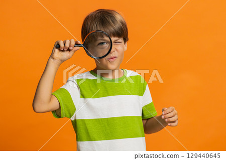 Child boy kid holds magnifying glass near face looking at camera with big zoomed eye, analyzing 129440645