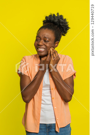 Black woman touching cheek closing eyes with expression of terrible suffer from painful toothache 129440719