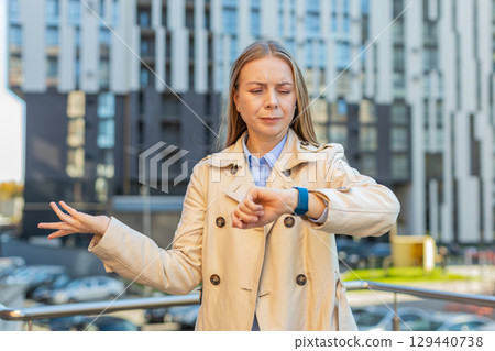Serious sad mature businesswoman standing outdoors looking around waiting for business meeting Serious sad mature businesswoman standing outdoors looking around waiting for business meeting 129440738