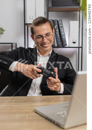 Excited young businessman playing video game on laptop with joystick controller at home office desk Excited young businessman playing video game on laptop with joystick controller at home office desk 129440740