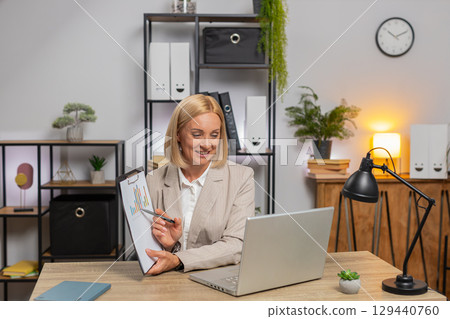 Mature businesswoman using laptop talking on online communication video call at home office desk 129440760