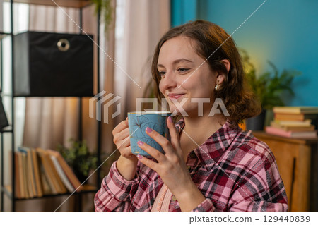 Businesswoman working on laptop computer drinking cup of warm hot coffee sit at table at home office Businesswoman working on laptop computer drinking cup of warm hot coffee sit at table at home office 129440839