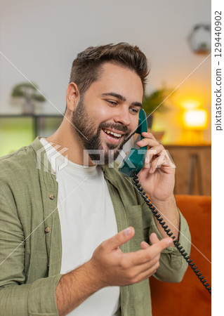 Smiling young man making wired telephone call conversation with friends sitting on sofa at home 129440902