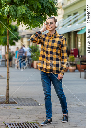 Happy young Caucasian man in wireless headphones dancing, listening music standing in city street Happy young Caucasian man in wireless headphones dancing, listening music standing in city street 129440905