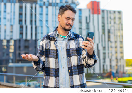 Upset mature man using smartphone browsing, loses becoming shocked bad news on downtown city street Upset mature man using smartphone browsing, loses becoming shocked bad news on downtown city street 129440924