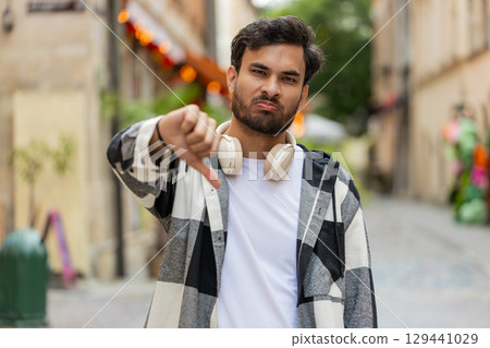 Upset Indian man showing thumb down sign gesture, expressing discontent disapproval in city street 129441029