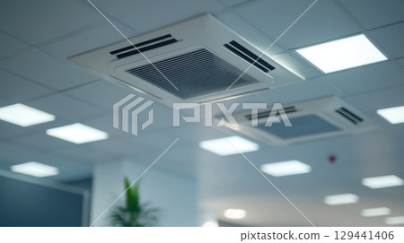 Ceiling air conditioning unit in a modern office setting with LED lights illuminating the workspace 129441406