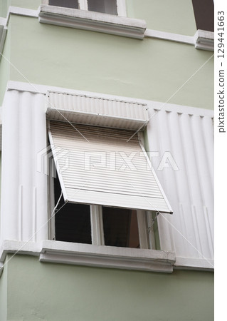 Window with rolled down shutters in a green building 129441663