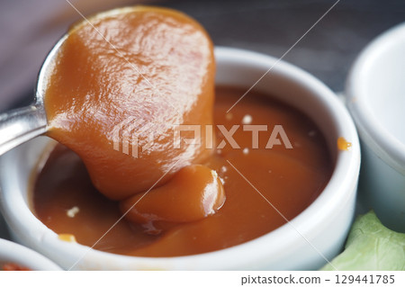 Rich caramel sauce in a small dish with spoon 129441785