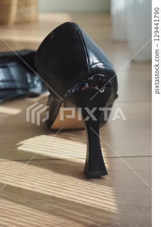 Black high heel shoe with damage on sunny wooden floor Black high heel shoe with damage on sunny wooden floor 129441790