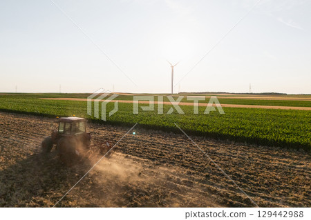 Agricultural tractor is working on the field with wind turbines. Aerial view. Agricultural tractor is working on the field with wind turbines. Aerial view. 129442988