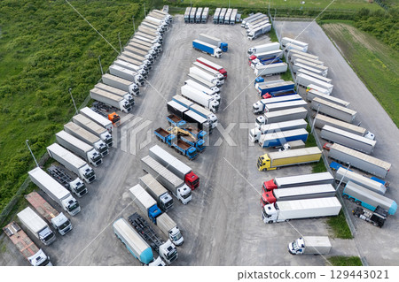 Aerial view of a large truck parking lot at a logistics hub, with multiple commercial semi trucks parked in organized rows. 129443021