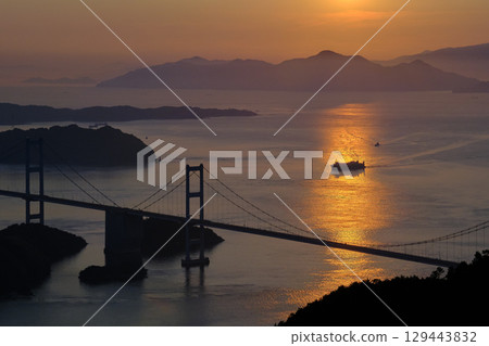 愛媛郡今治市:夕陽將大海染成紅色,一艘船駛近連接本州和四國的來島海峽大橋。 愛媛郡今治市:夕陽將大海染成紅色,一艘船駛近連接本州和四國的來島海峽大橋。 129443832