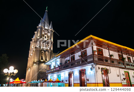 The illuminated Basilica of the Immaculate Conception and a traditional colonial building at night in the main square of Jardin, Colombia 129444098