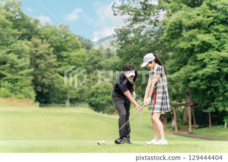 A male golfer teaching golf at a golf course and a female golfer hitting a tee shot A male golfer teaching golf at a golf course and a female golfer hitting a tee shot 129444404