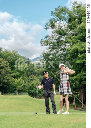 A male golfer teaching golf at a golf course and a female golfer hitting a tee shot 129444406