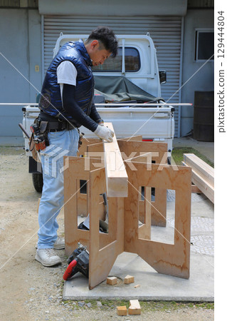 A carpenter standing and working with wood on a workbench, full body 129444804
