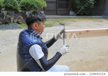 一位木匠正在用彎尺測量一塊木頭的側面長度（腰部以上） 129445154