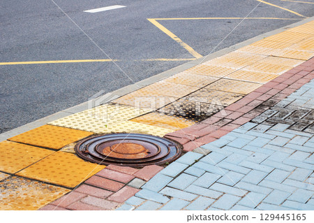 A round manhole cover is situated on the sidewalk beside the road 129445165