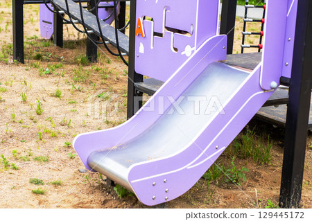 A vibrant purple and silver slide situated in a playground area 129445172
