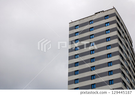 A tall building with many windows against a cloudy sky 129445187