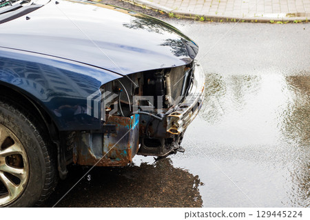 A damaged car from an accident is in a puddle of water A damaged car from an accident is in a puddle of water 129445224