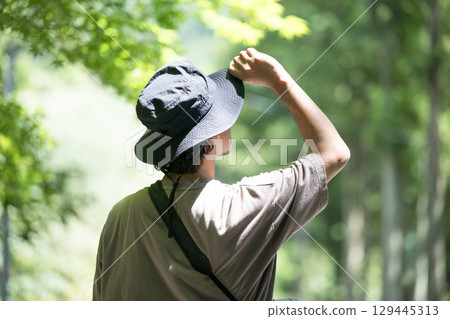 Back view of a man wearing a hat looking at greenery in the forest or camping, no face 129445313