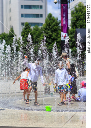 Children enjoying splashing around in the fountain in midsummer 129445971