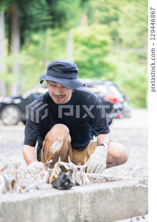 一名男子在露營地烤魚。戶外活動包括汽車露營和釣魚。 一名男子在露營地烤魚。戶外活動包括汽車露營和釣魚。 129446867