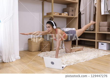 Young Sport Women look at laptop online trainer home fitness workout exercise in living room. Woman using laptop on floor in sportswear arms stretching body weight traning. Healthy lifestyle concept Young Sport Women look at laptop online trainer home fitness workout exercise in living room. Woman using laptop on floor in sportswear arms stretching body weight traning. Healthy lifestyle concept 129447276