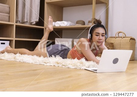 Young Sport Women look at laptop online trainer home fitness workout exercise in living room. Woman using laptop on floor in sportswear arms stretching body weight traning. Healthy lifestyle concept 129447277