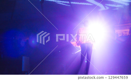 An unrecognized fashion model walks confidently on stage under bright lights, showcasing vibrant outfit and dynamic movement in an energetic atmosphere 129447659