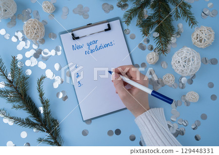 Female hands writing handwritten new year resolutions aims goals on paper notepad. Preparation for New Year. Planning and setting goals for personal development  129448331
