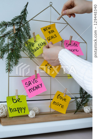 Female hands creating vision board with new year resolutions aims goals on sticky notes. Preparation for New Year. Planning and setting goals for personal development  129448340